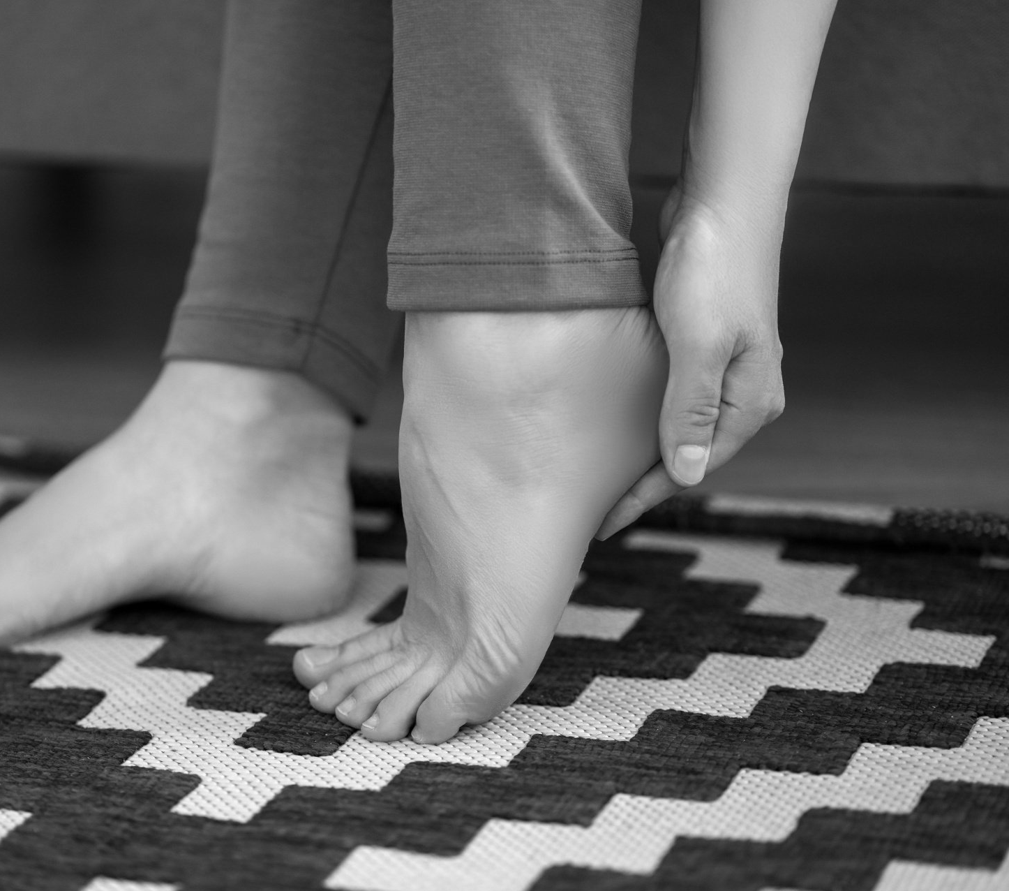 black and white close up photo of a woman feet. the woman is touching the bottom of her heel because of discomfort