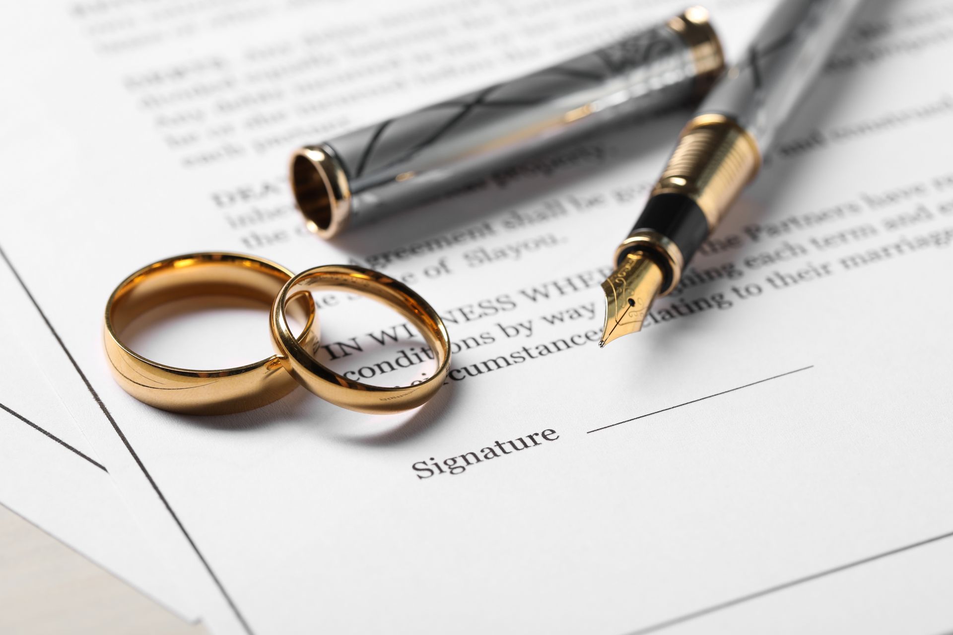 A pair of wedding rings and a fountain pen on a piece of paper.