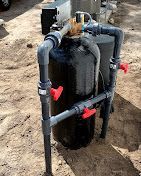 A black tank with red valves attached to it is sitting on top of a pile of dirt.