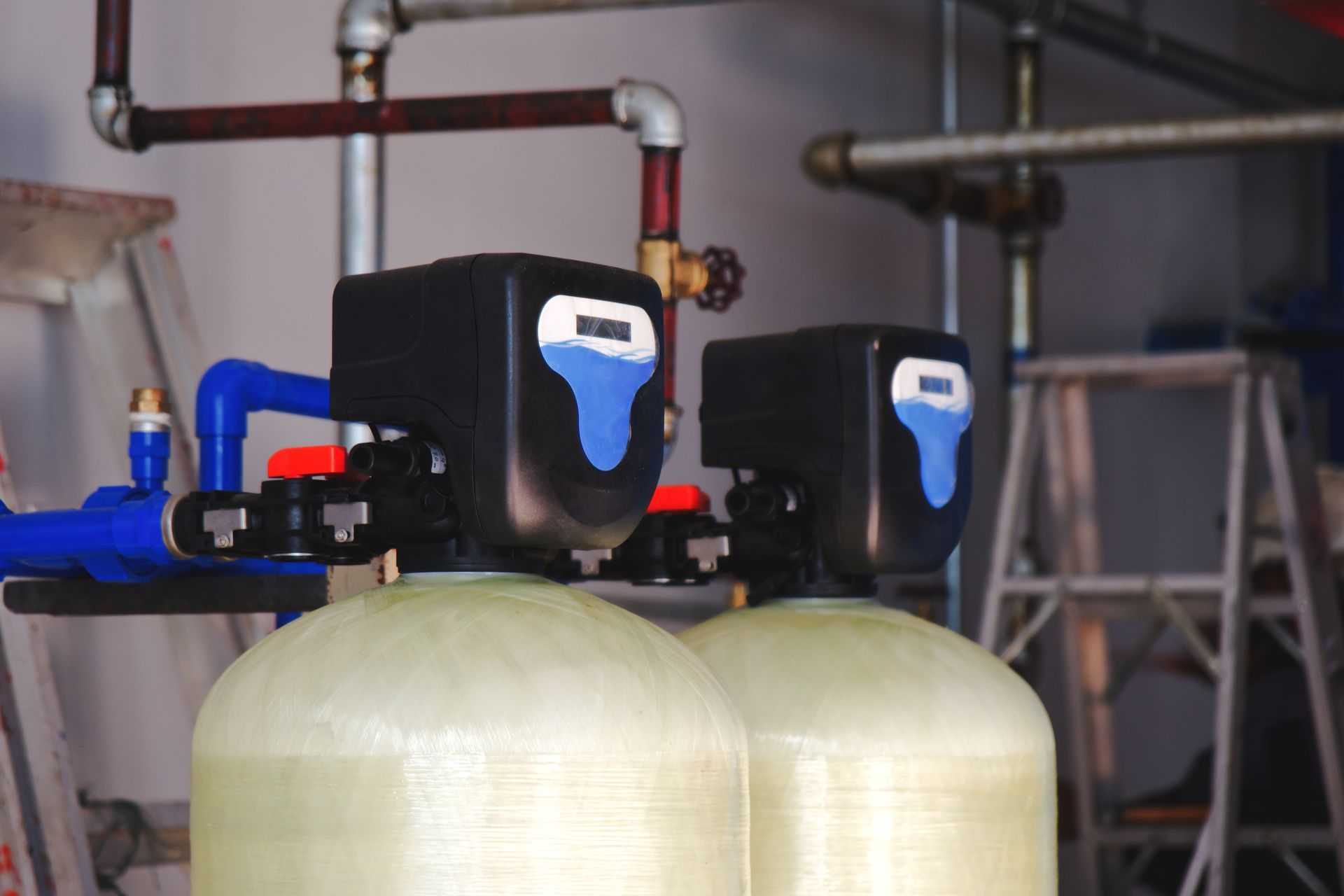 Dual water filtration tanks connected to pipes in a utility room for household water treatment.