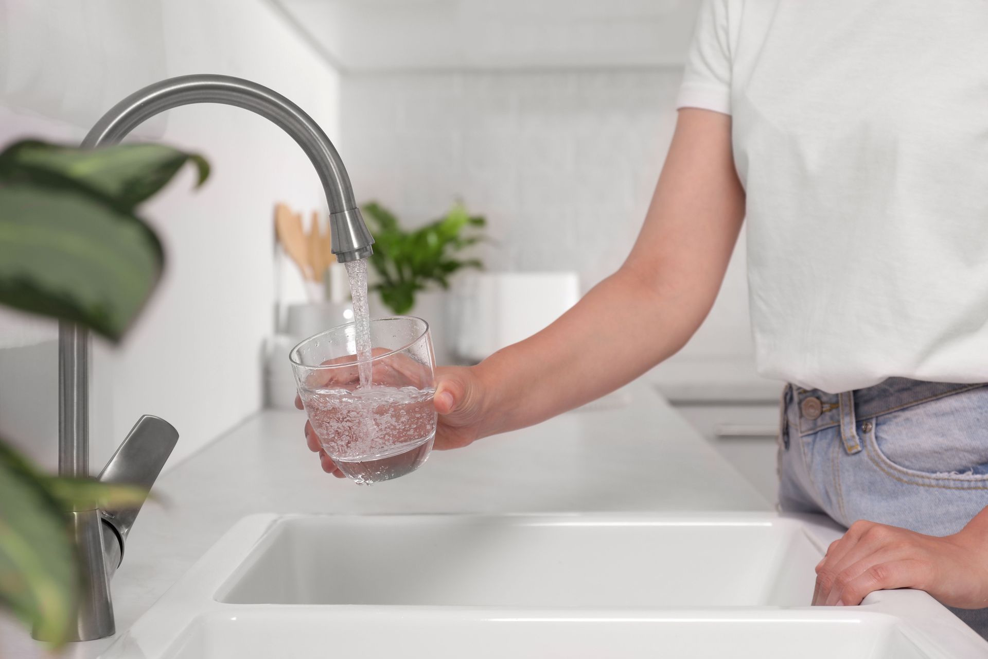 Woman filling glass with water from tap in kitchen.