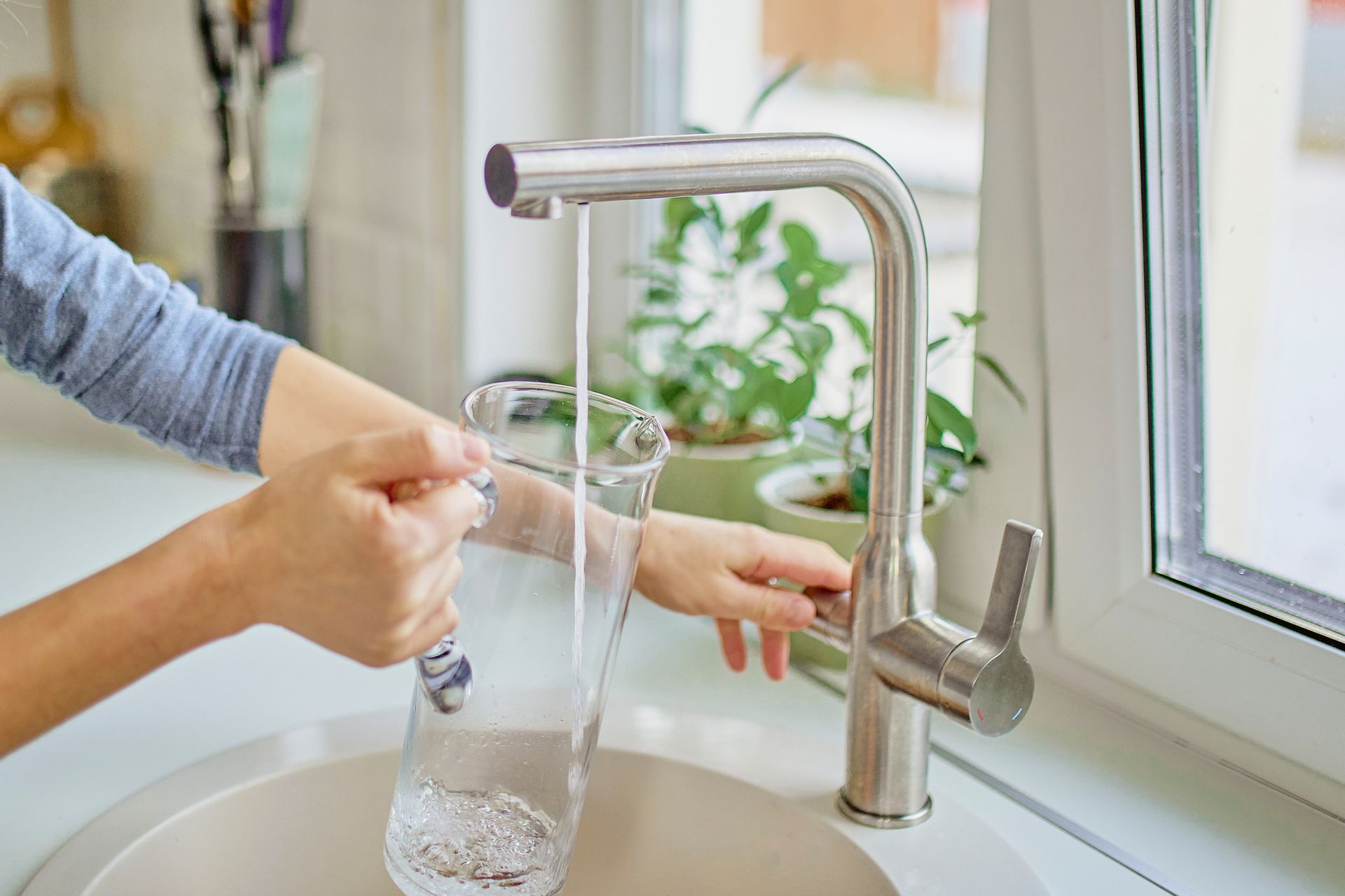 Person filling a glass pitcher with water from a kitchen faucet. Person filling a glass pitcher with water from a kitchen faucet.