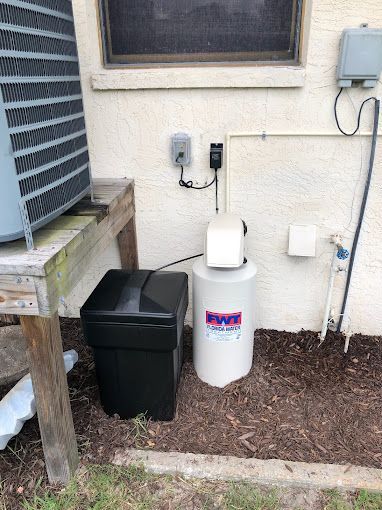 A water softener is sitting outside of a house next to a window.