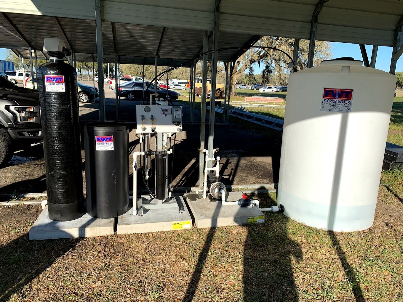 A water treatment system is sitting under a canopy in a parking lot.