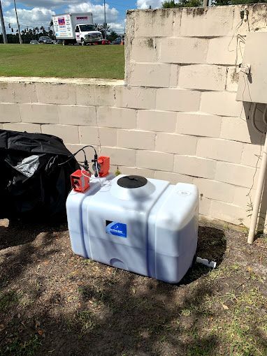 A large white tank is sitting on the ground next to a brick wall.
