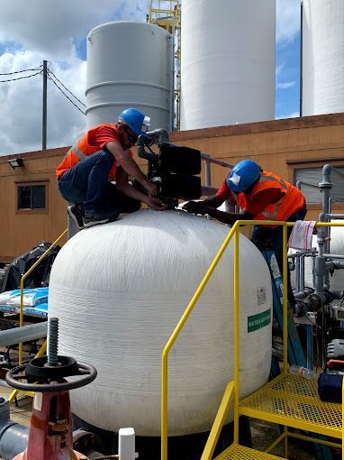 Two men are working on a large white tank in a factory.