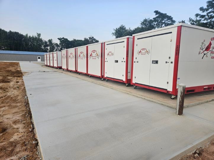 Two white storage containers with blue roll-up doors in a parking lot on a sunny day.