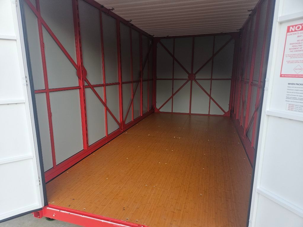 Two white storage containers with blue roll-up doors in a parking lot on a sunny day.