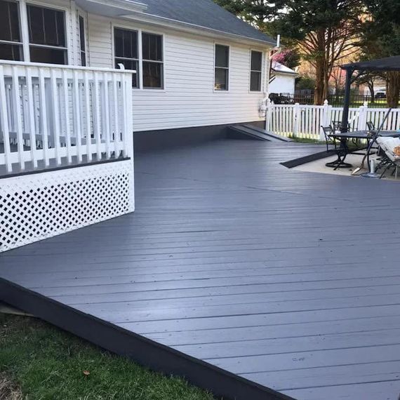 Gray-painted wooden deck attached to a white house with a white railing. Black ramp on the side.