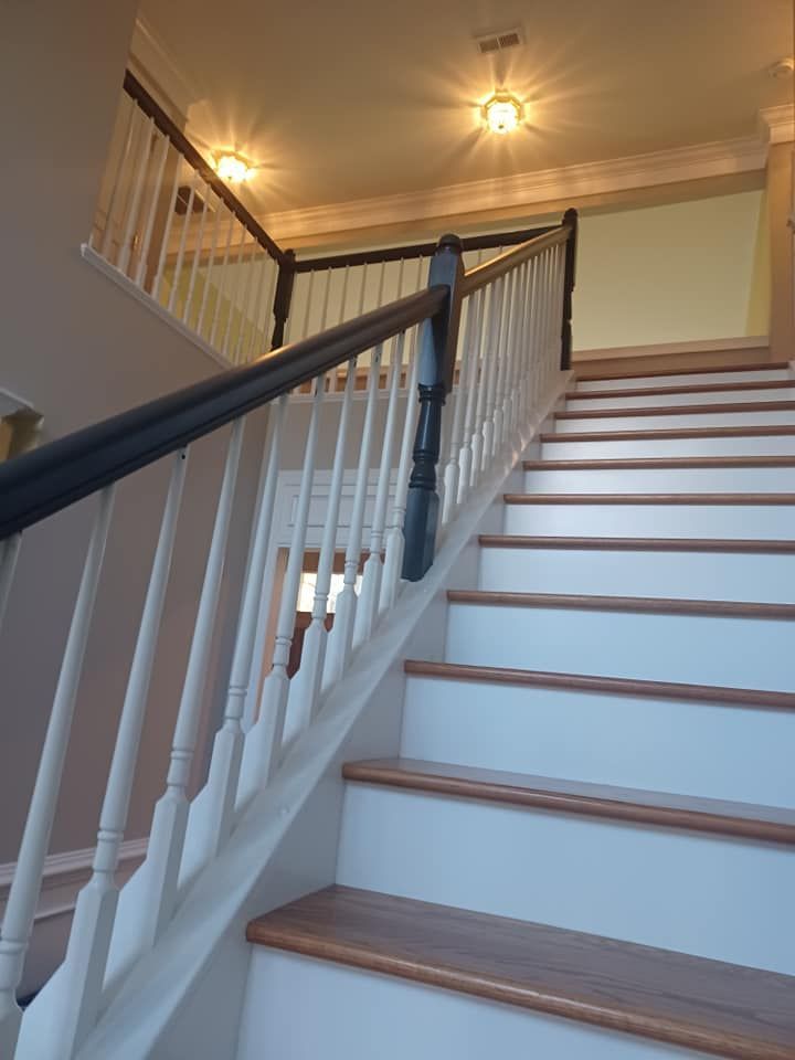 Staircase with white risers and wood treads. Black handrails, white balusters, and overhead lighting.