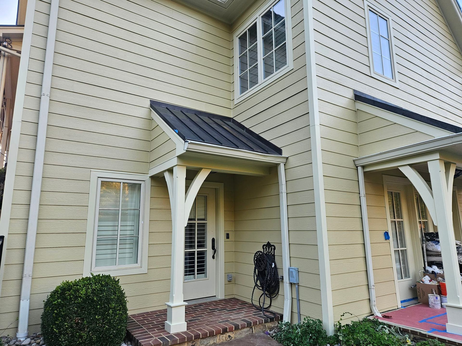 Beige house with a black metal awning over a brick entrance and white trim.