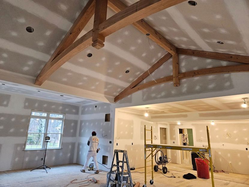 Interior view of room under construction with exposed wooden beams, drywall, and a person working.