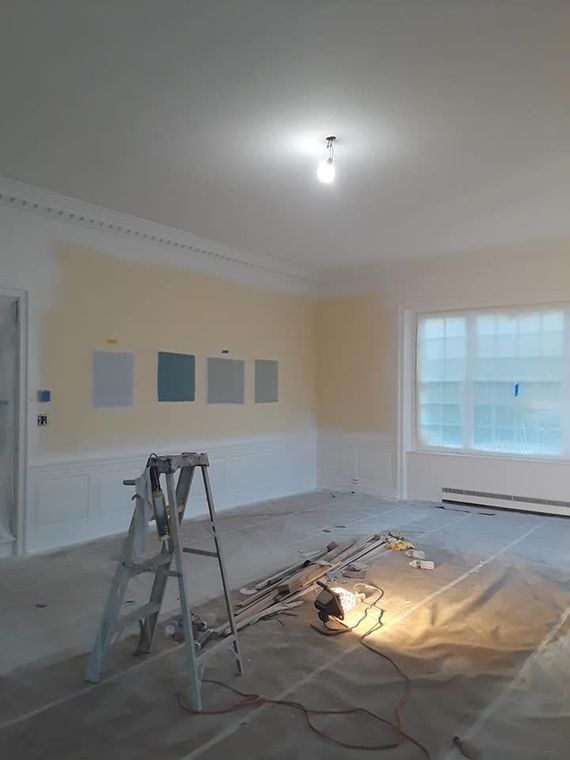 Room under renovation with paint swatches, ladder, drop cloth, and exposed wiring.