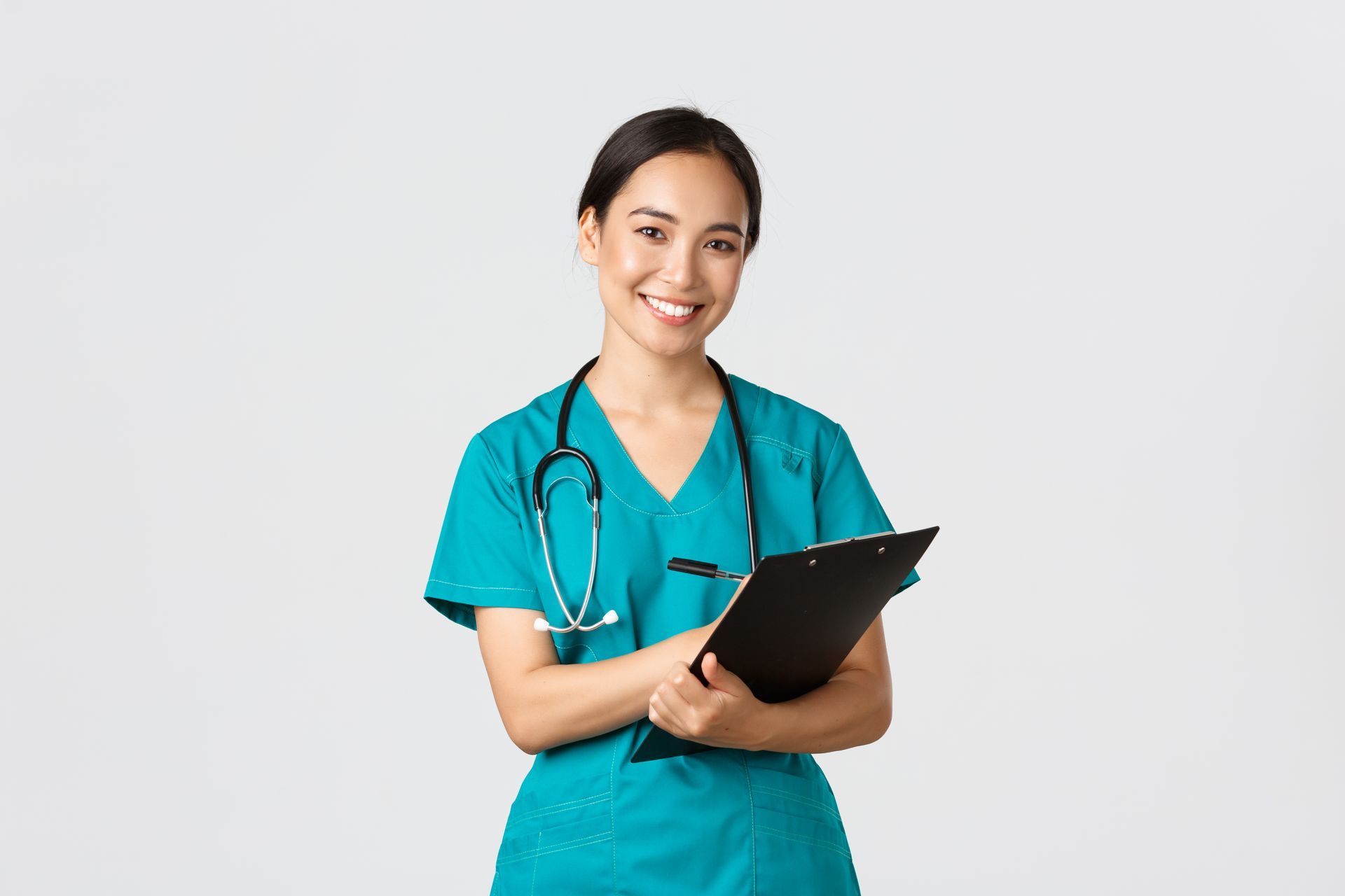 A nurse with a stethoscope around her neck is holding a clipboard and smiling.