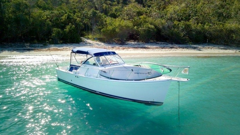 A white boat is floating on top of a body of water near a beach.