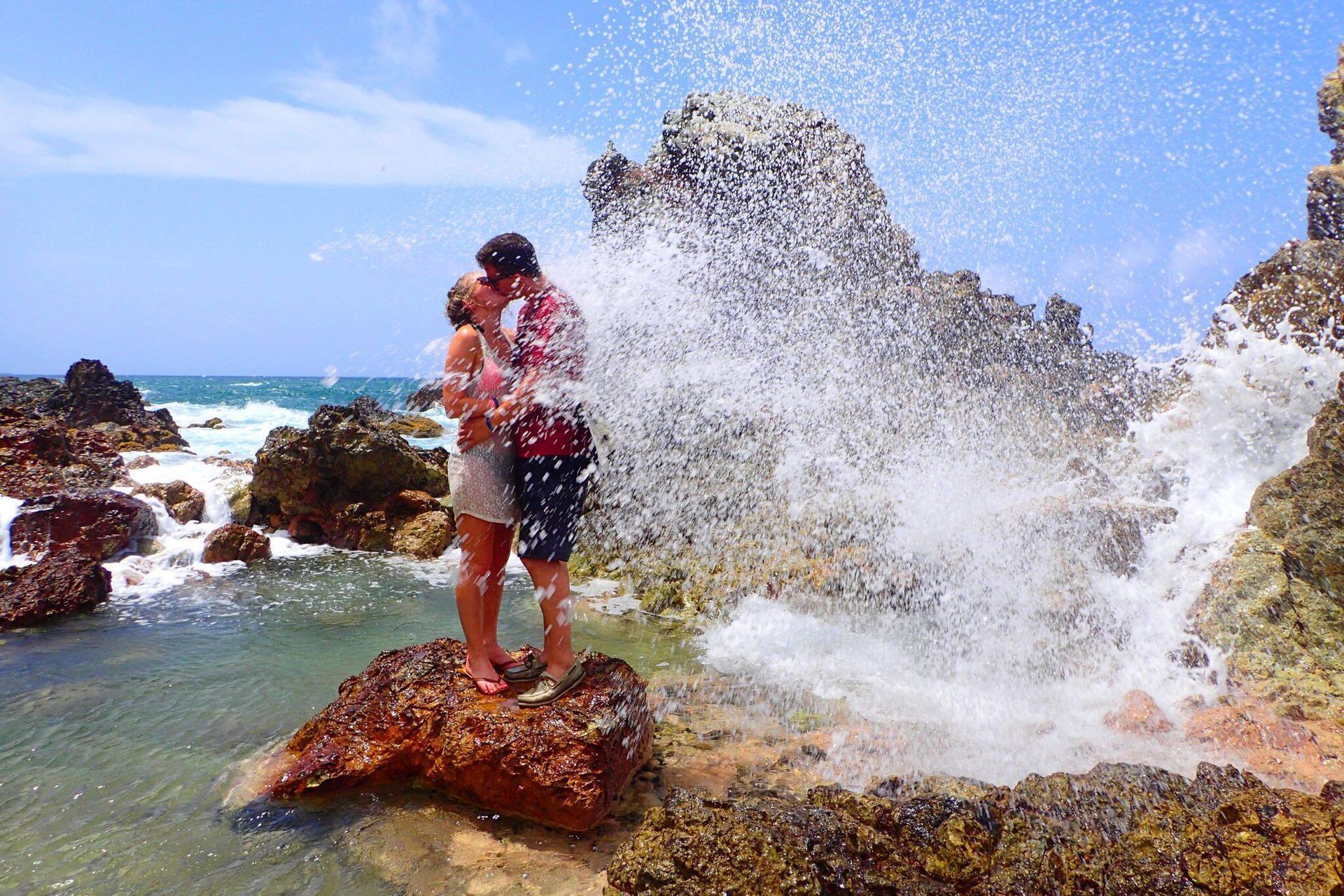 A man and woman are kissing on a rock near the ocean.