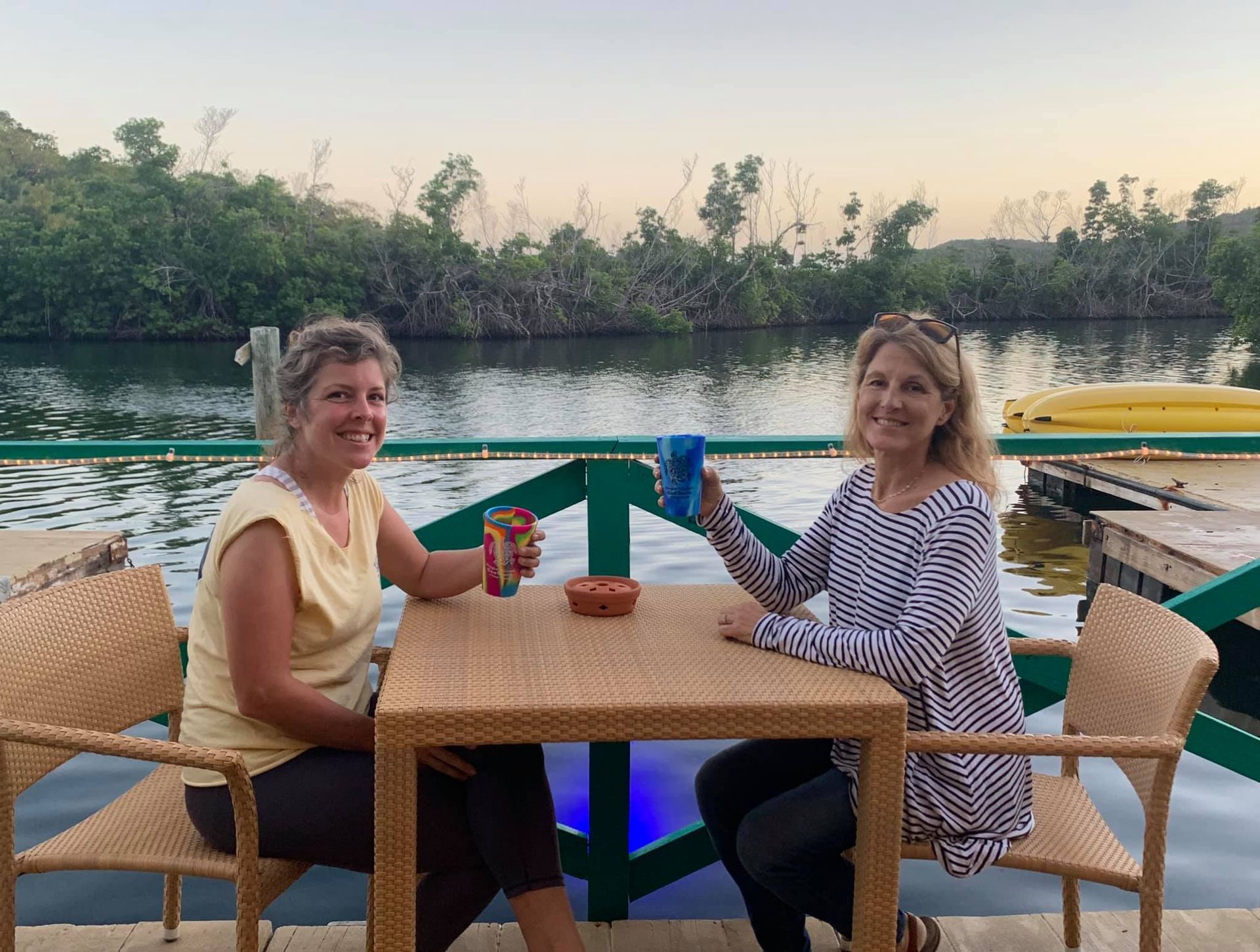 Two women are sitting at a table in front of a body of water.