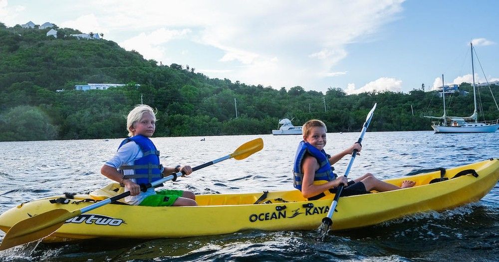 Two kids are paddling yellow kayaks in the water.