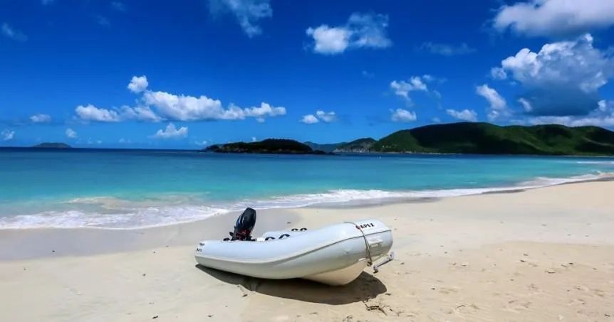 A boat is sitting on a sandy beach next to the ocean.