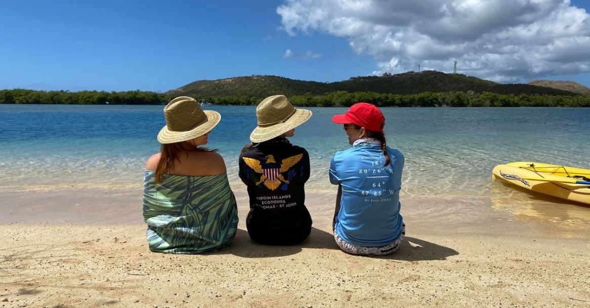 Three people are sitting on the beach looking at the water.