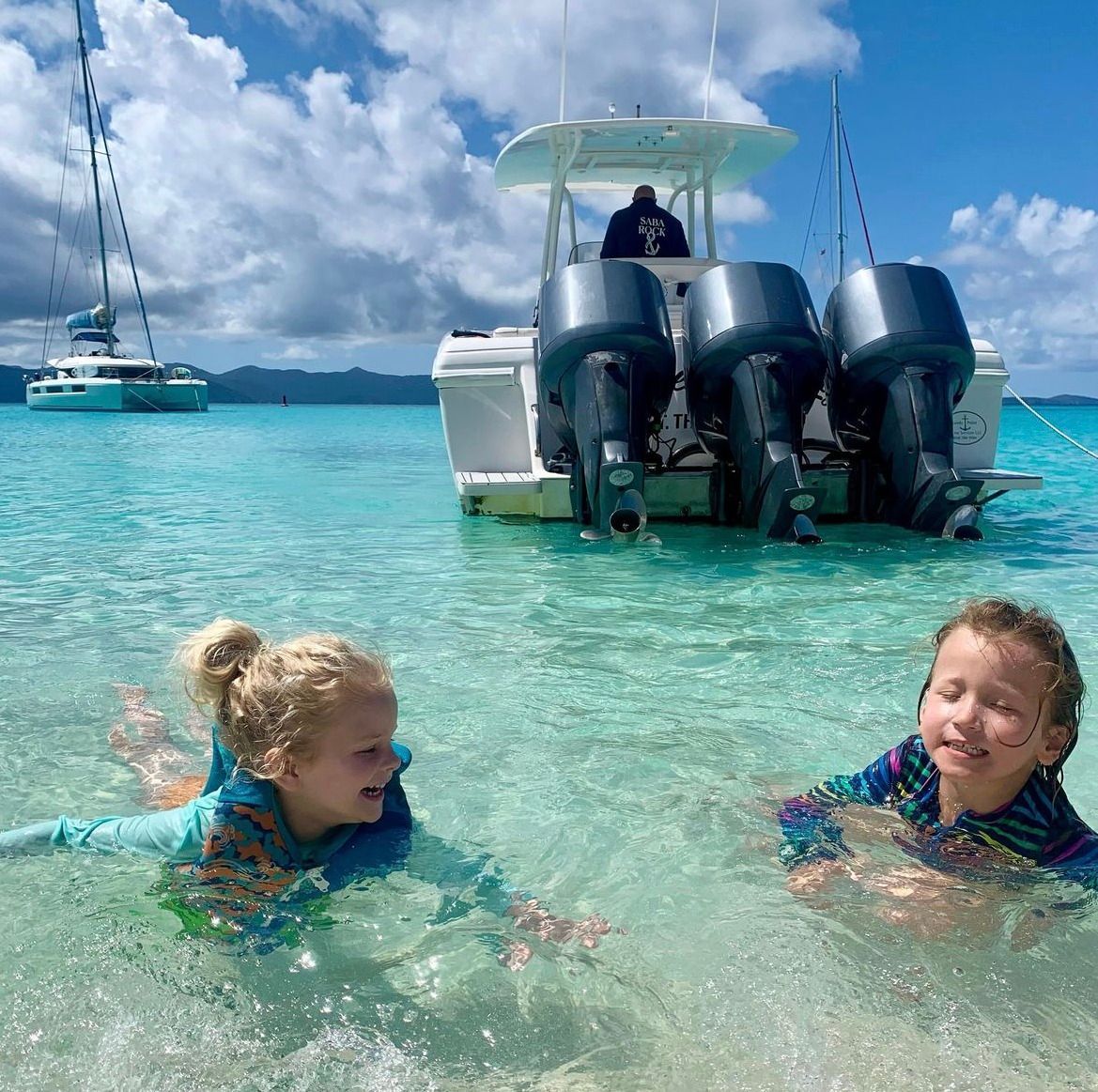 Two children are swimming in the ocean with a boat in the background