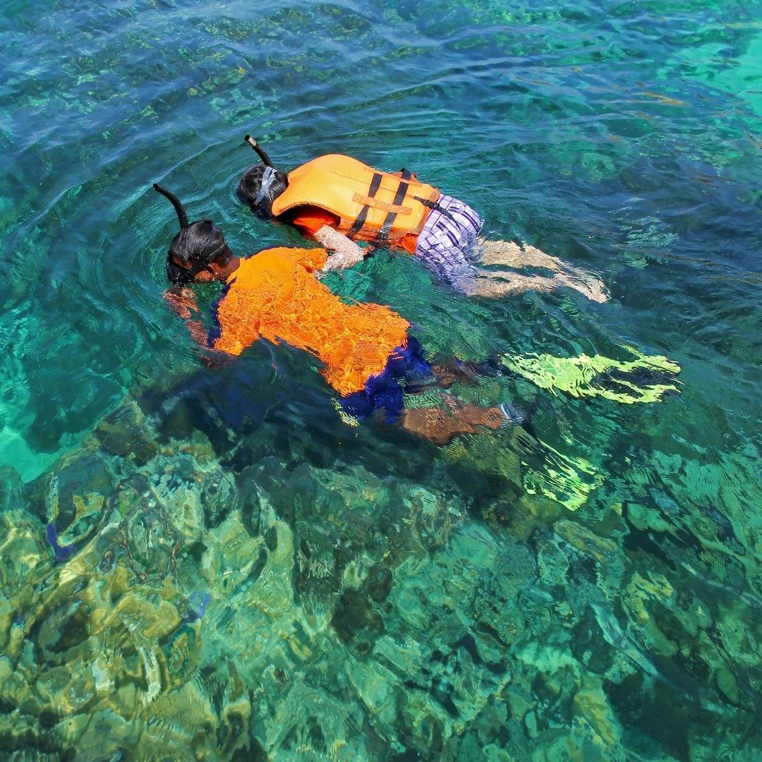 Two people are swimming in the ocean wearing life jackets and flippers.