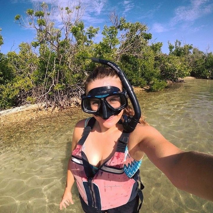 A woman wearing a mask and snorkel is taking a selfie in the water.