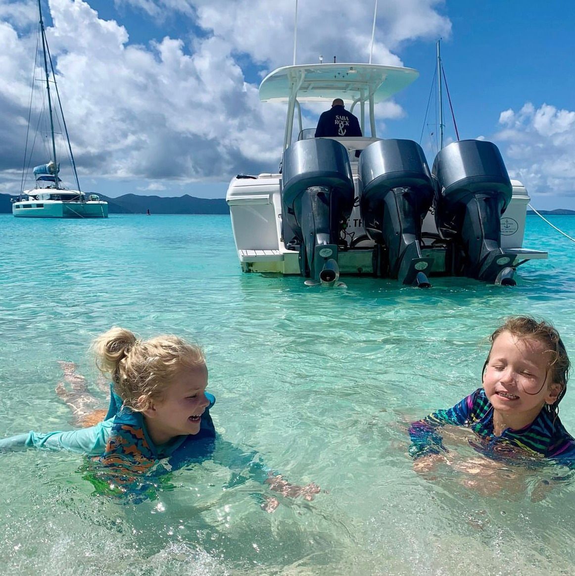 Two children are swimming in the ocean with a boat in the background.