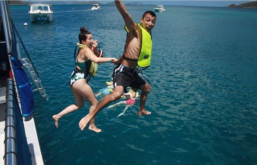 A man and a woman are jumping into the water from a boat.