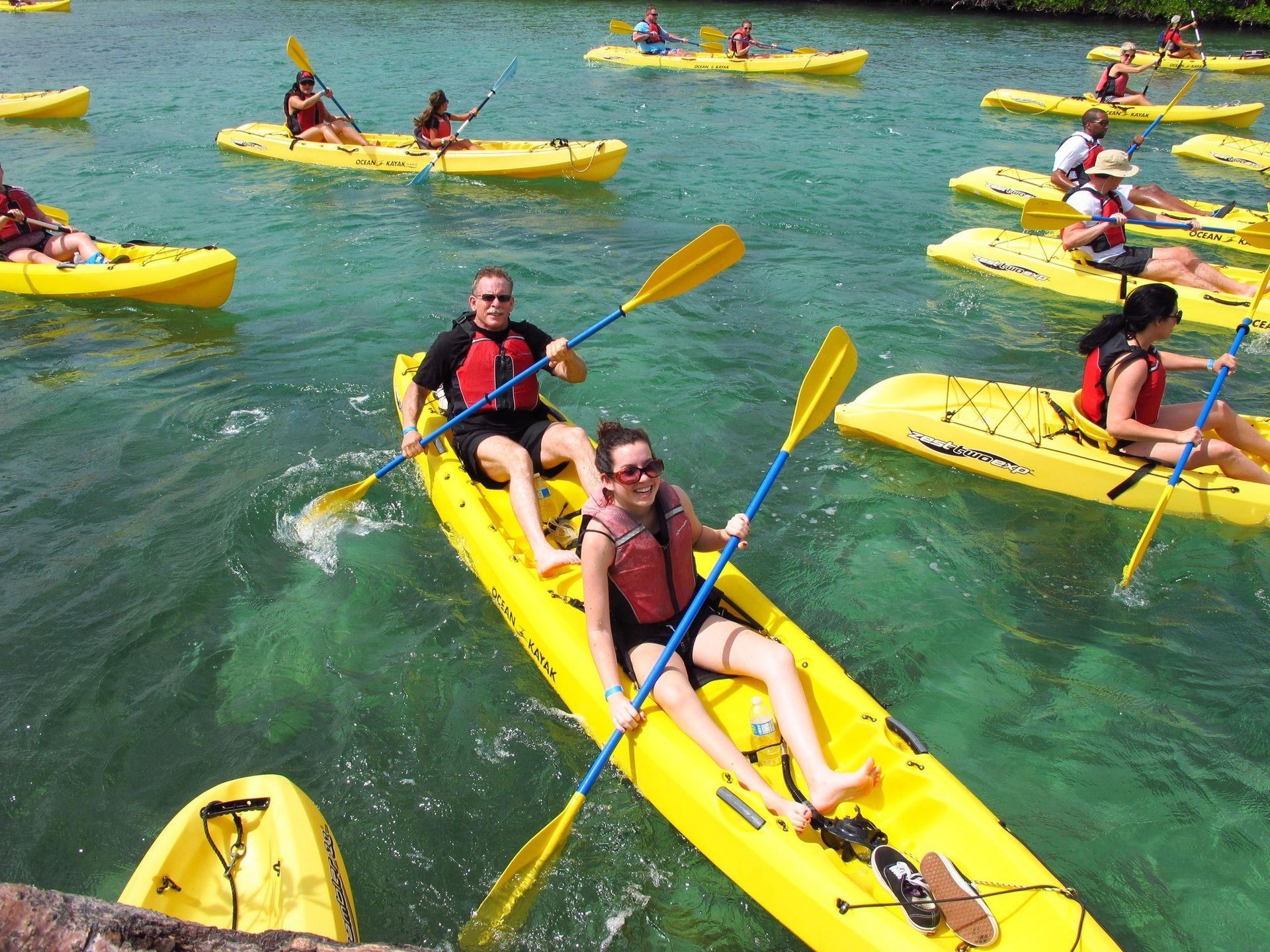 A group of people are paddling yellow kayaks in the water