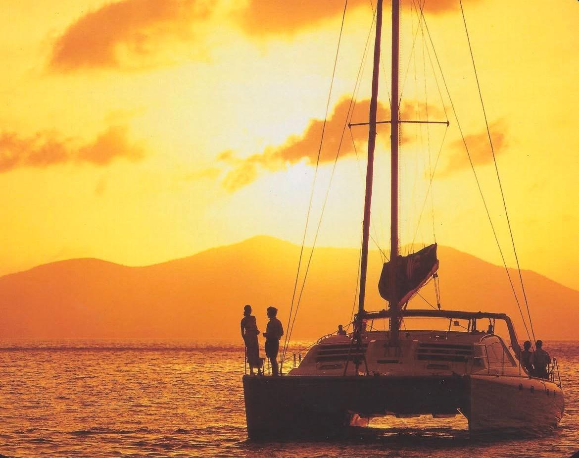 Two people standing on a boat in the ocean at sunset