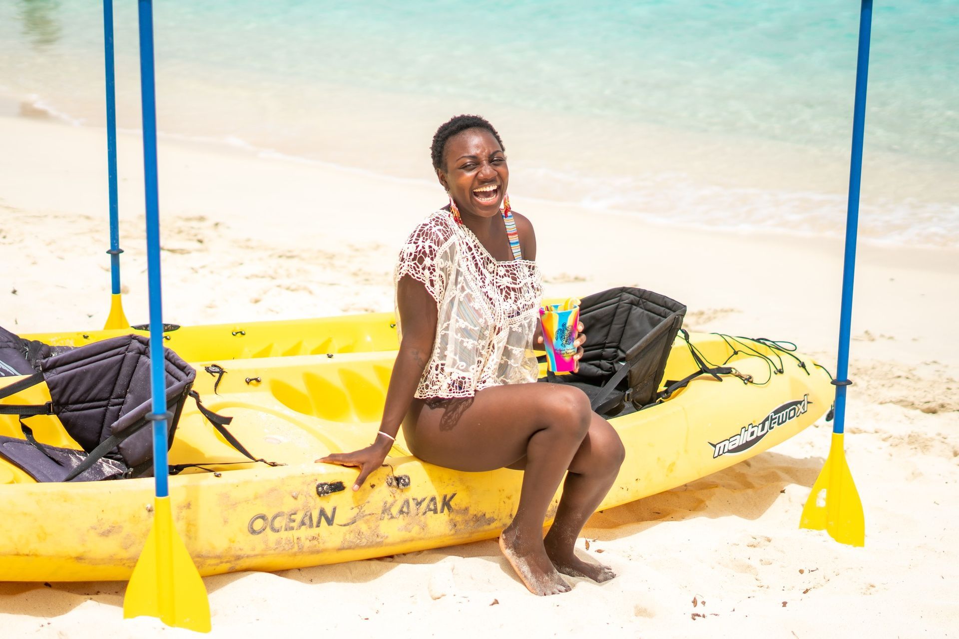 A woman is sitting on a yellow kayak on the beach.