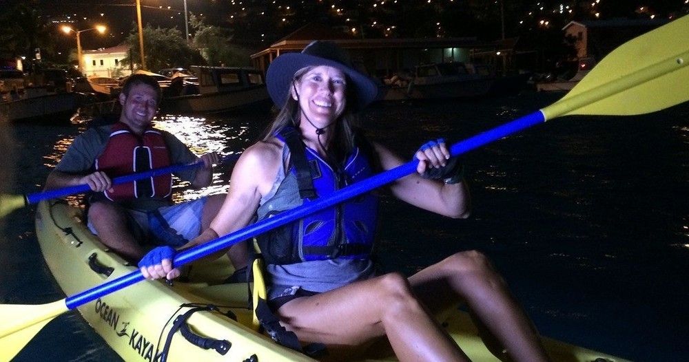 A man and a woman are paddling kayaks in the water at night