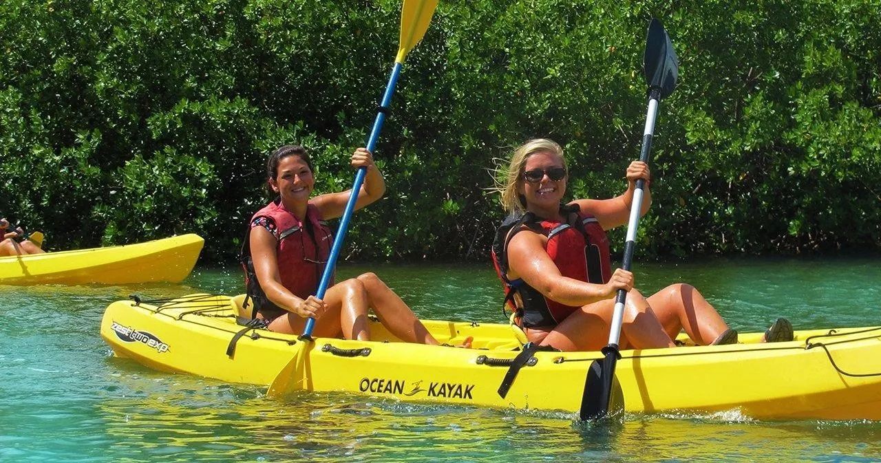 Two women are paddling yellow kayaks in the water.