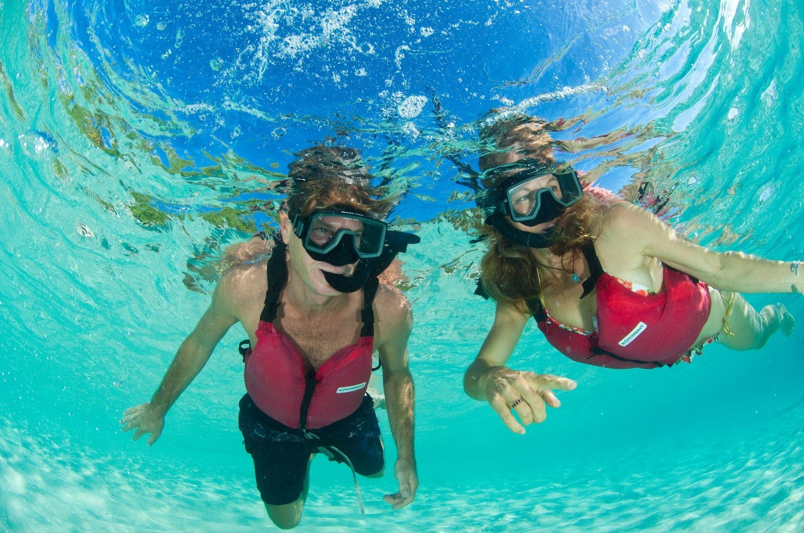 Two people snorkeling underwater in clear turquoise water.