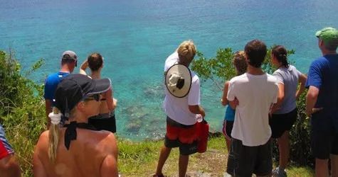 A group of people are standing on a hill overlooking the ocean.