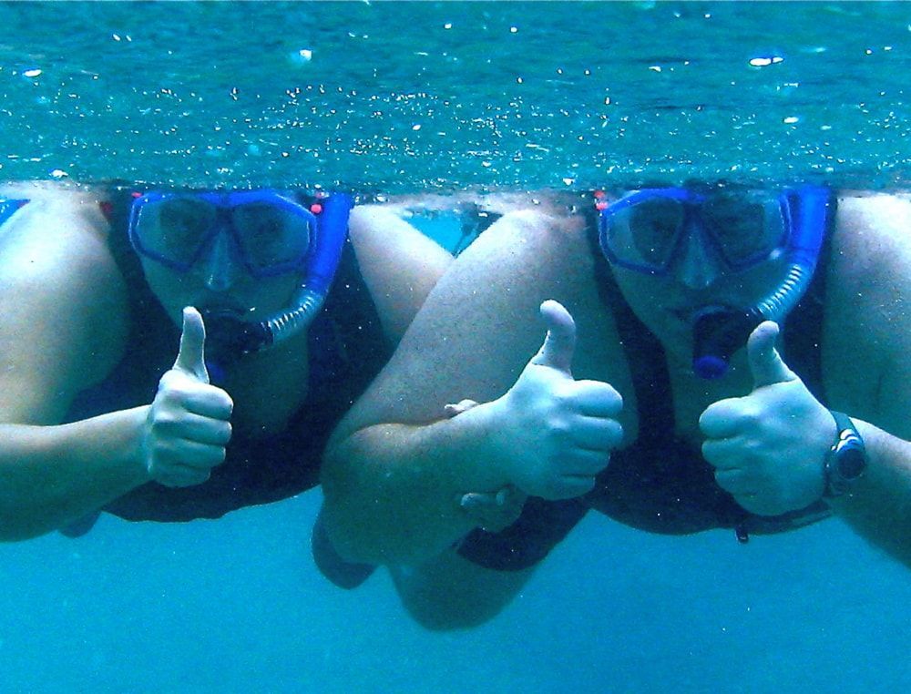 Two people snorkeling, giving thumbs up underwater.
