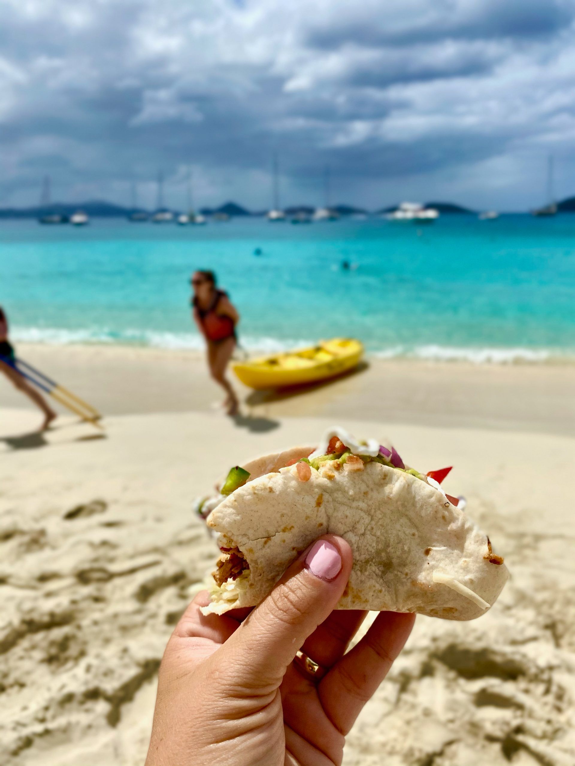 A person is holding a taco on the beach