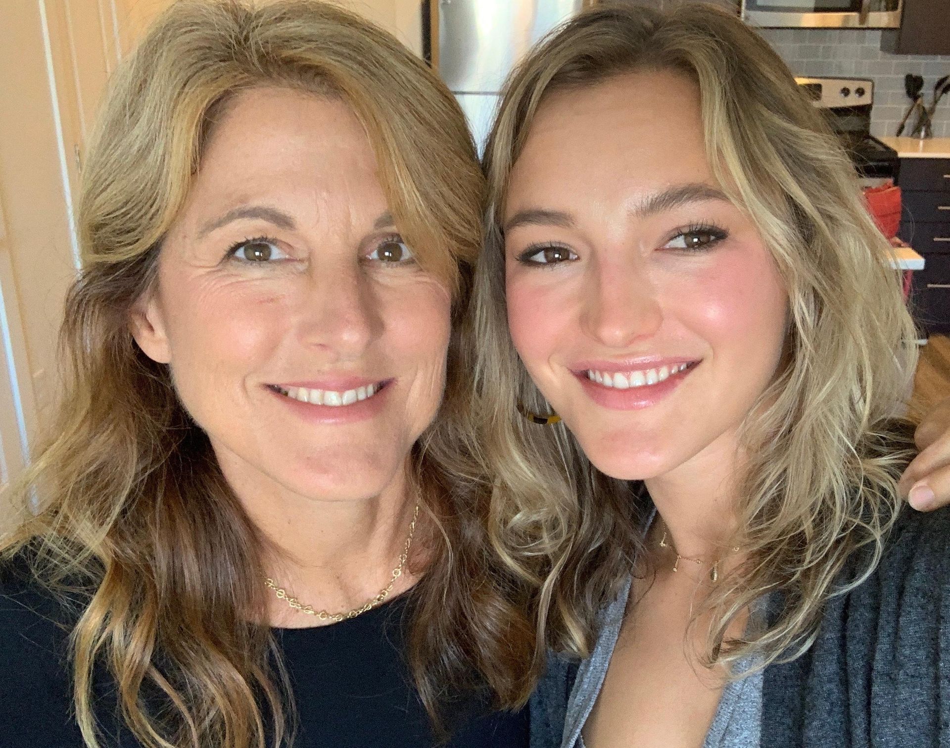 A mother and daughter are posing for a picture together in a kitchen.