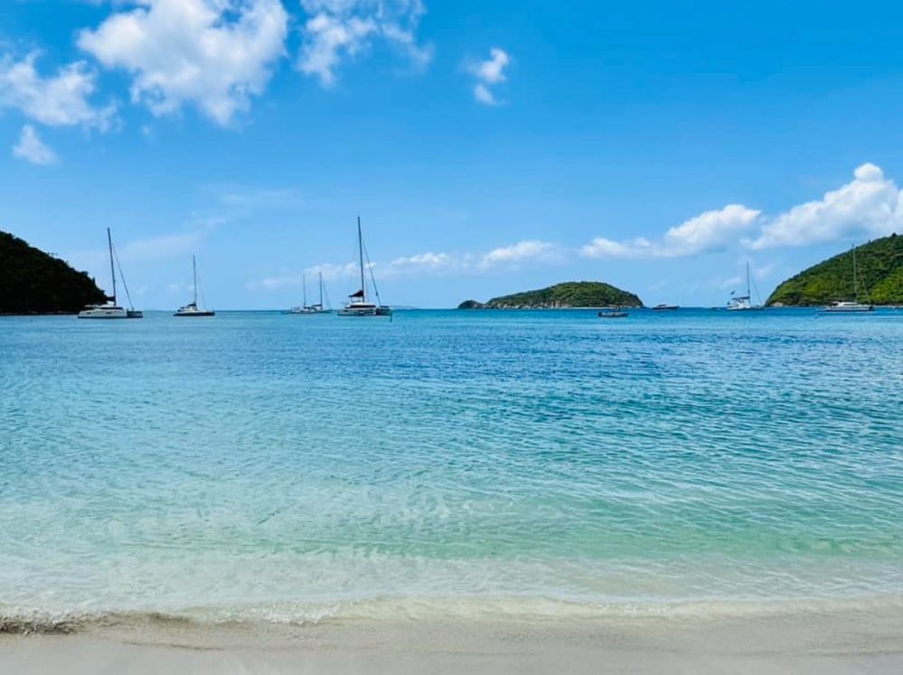 A beach with boats in the water and a blue sky