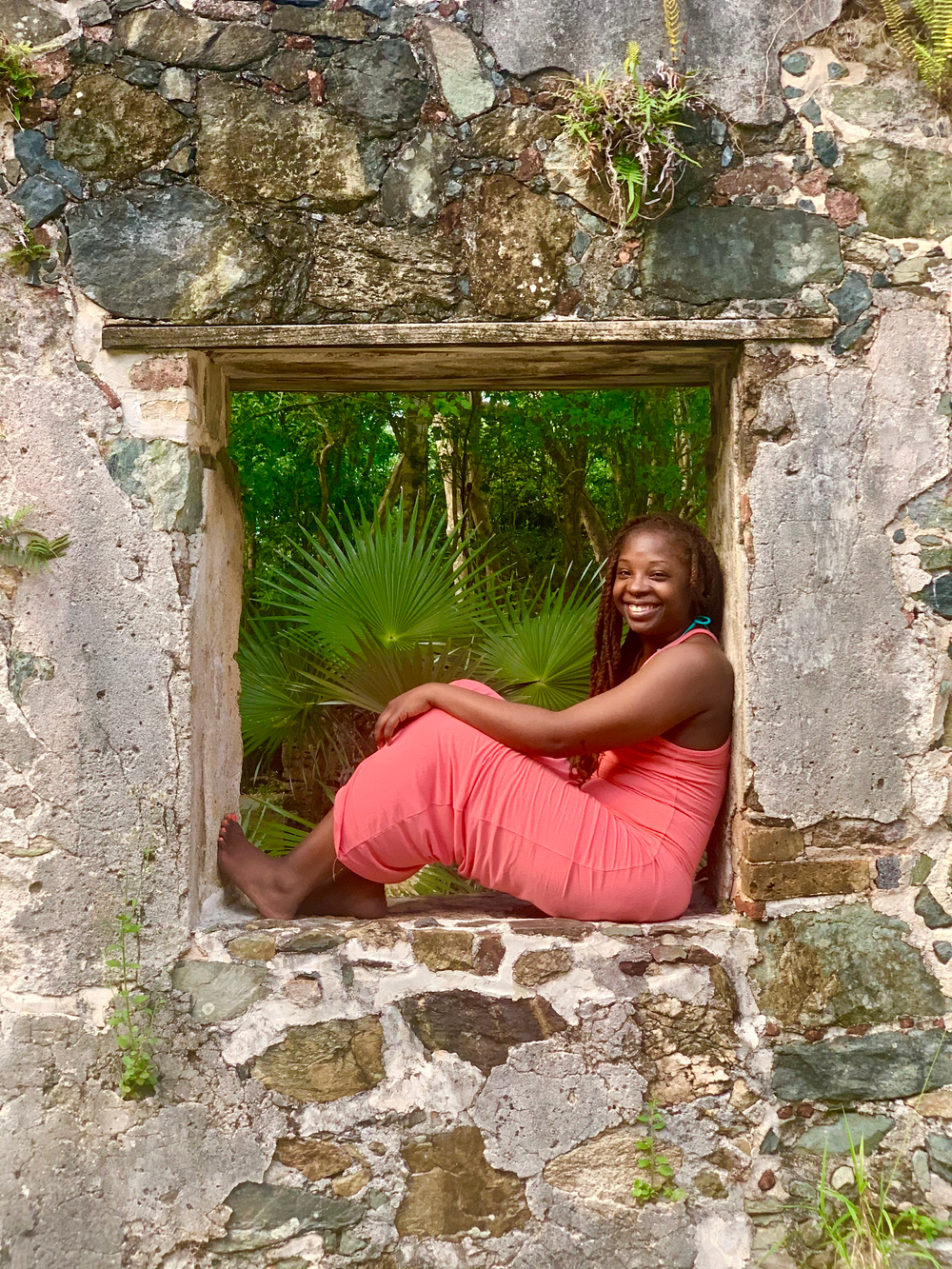 A woman in a pink dress is sitting in a stone window.