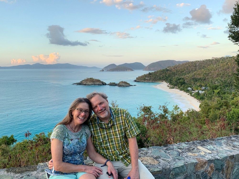 A man and a woman are sitting on a rock overlooking the ocean.