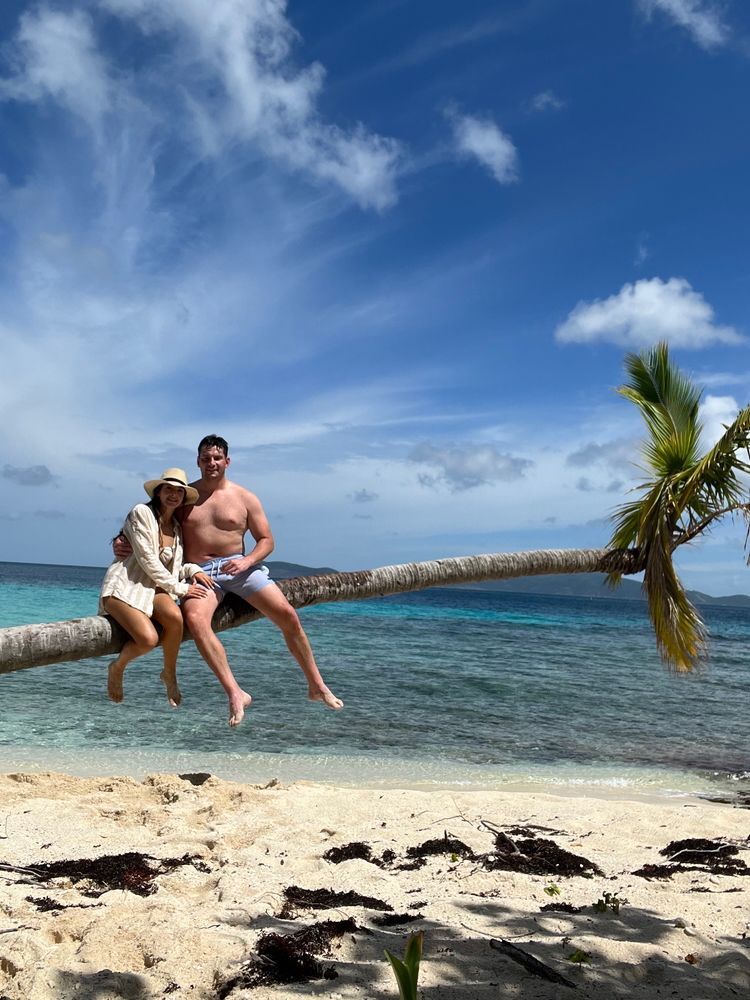 A man and a woman are sitting on a palm tree branch on a beach.