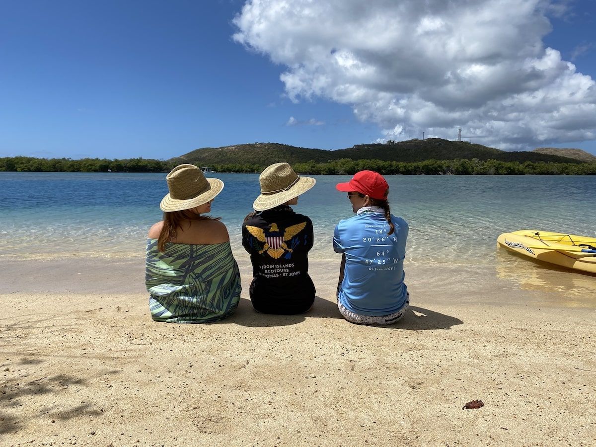 Three people are sitting on the beach looking at the water.