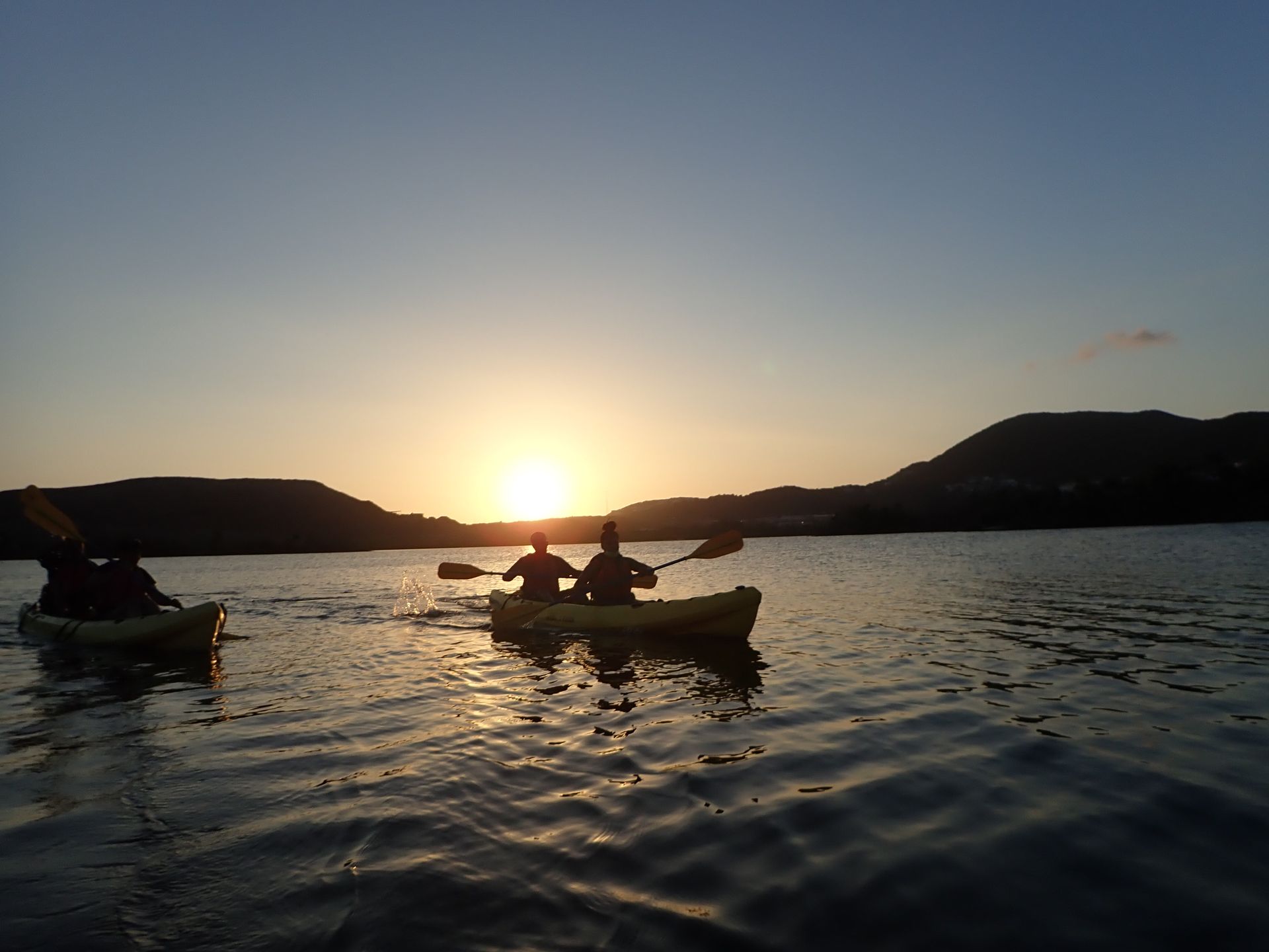 A group of people in kayaks on a lake at sunset