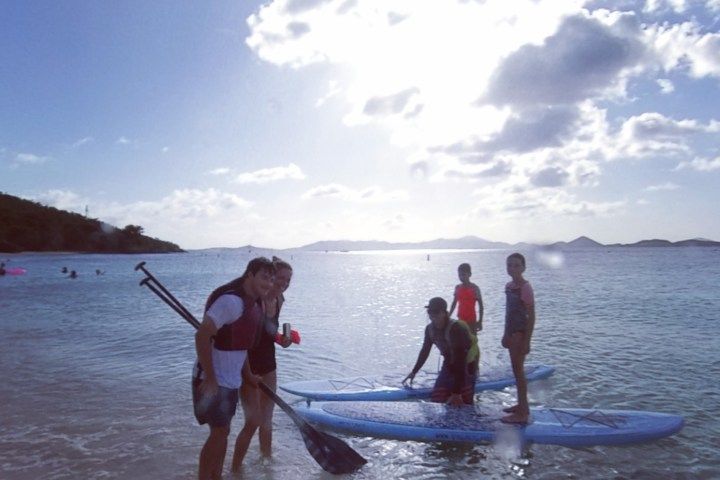 A group of people are standing on a beach with paddle boards in the water.