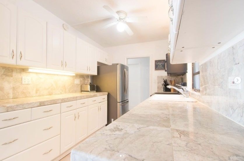 A kitchen with white cabinets and marble counter tops.