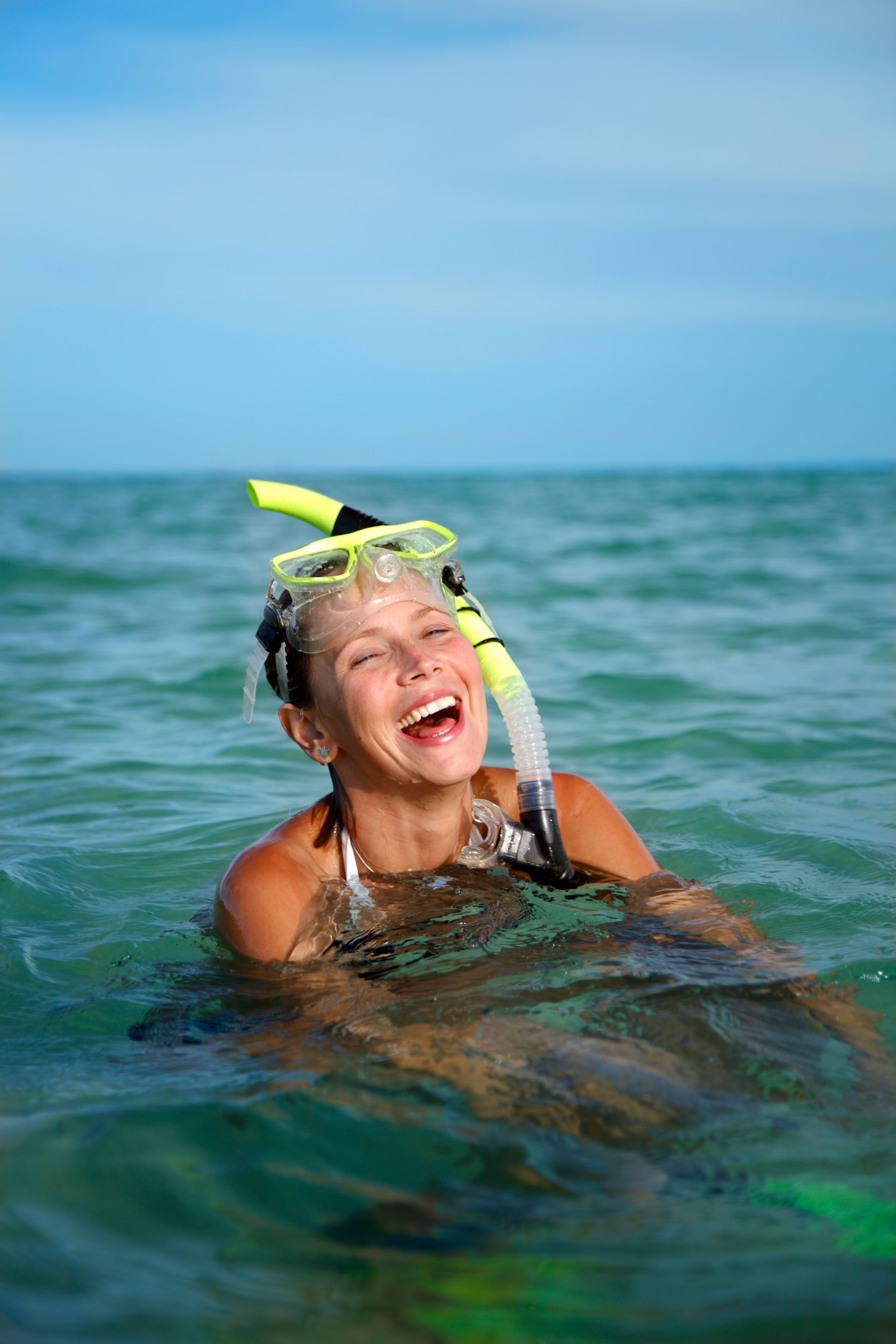 Woman snorkeling, laughing in clear blue ocean water with snorkel gear.