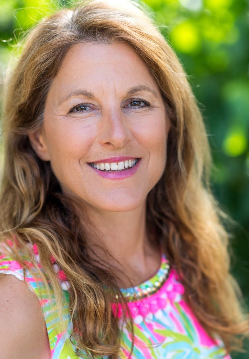 A woman in a pink and green dress is smiling for the camera.