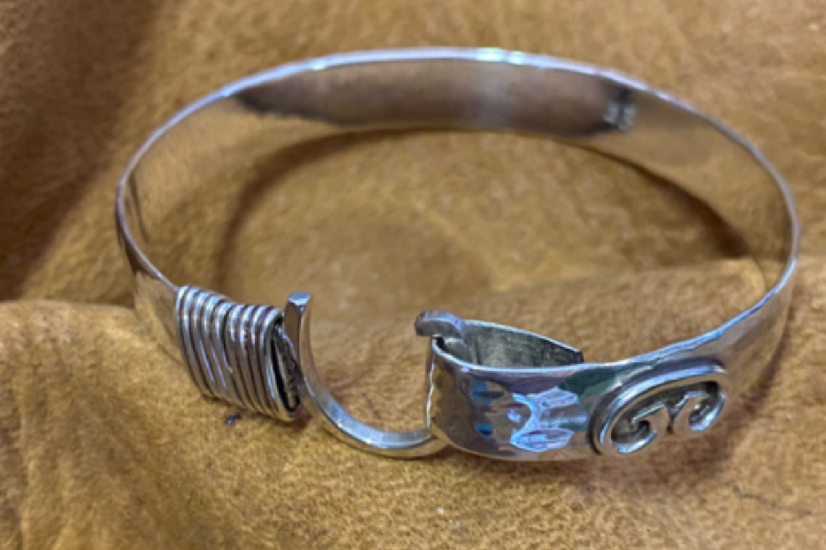 A silver bracelet made out of a fork is sitting on a brown cloth.